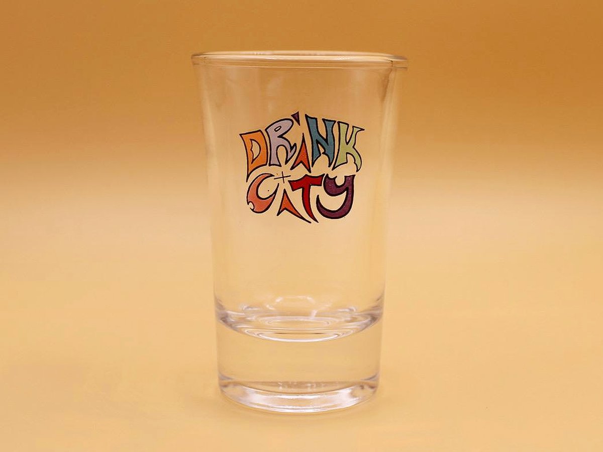 Drink City Shotglas vor goldenem Hintergrund