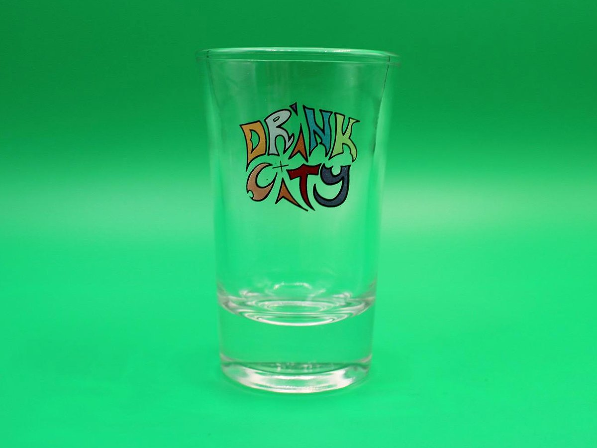 Drink City Shotglas vor grünem Hintergrund